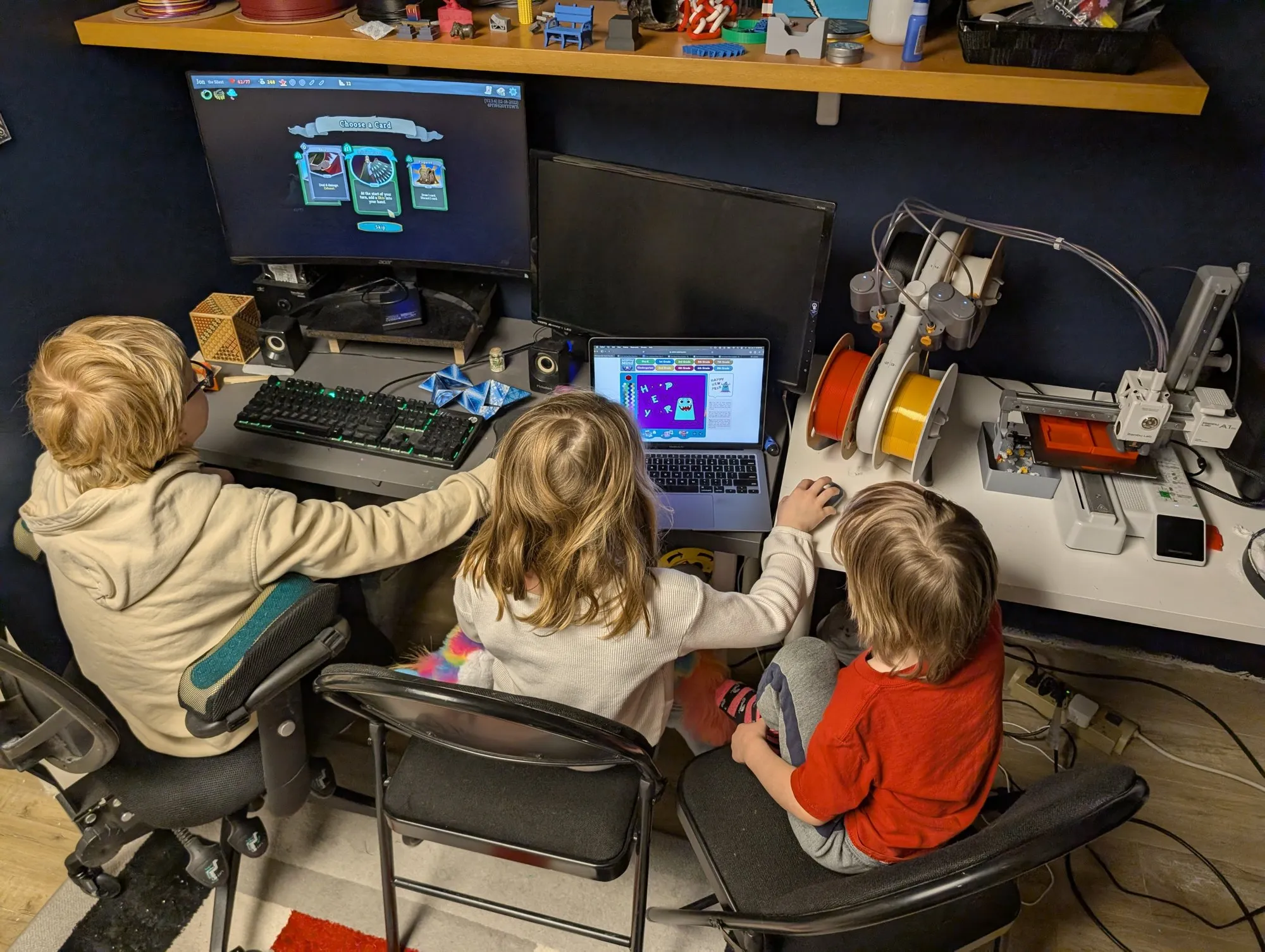 Three kids at a desk watching a 3D printer and a computer